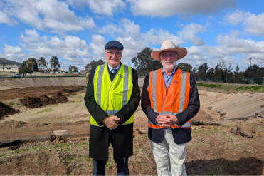 Vice Chancellor of UNE and Mayor of Tamworth region standing in foreground with demolition works underway in background, fetauring the velodrome site with dirt being turned in the middle