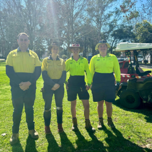 Four trainees in hi vis standing in a park with zero turn mower in the background